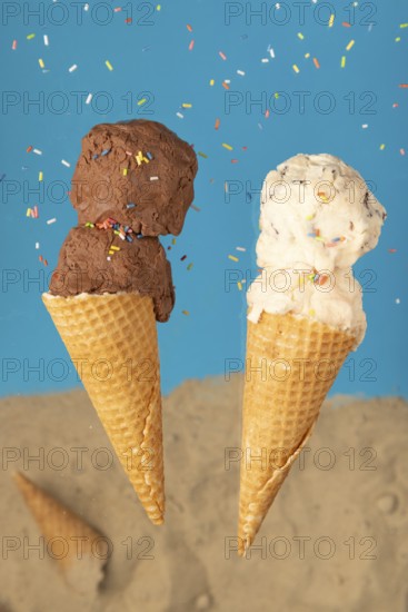 Two ice cream cones, one with chocolate ice cream and one with cream ice cream, against a blue background with sprinkles