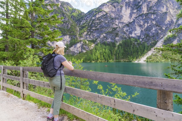 Person looking from a wooden fence at a mountain lake, surrounded by nature, Lake Braies, South Tyrol, Dolomites, Italy