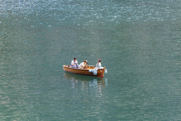 Three people in a small wooden boat on a quiet lake enjoying a relaxing trip, Lake Braies, South Tyrol, Dolomites, Italy