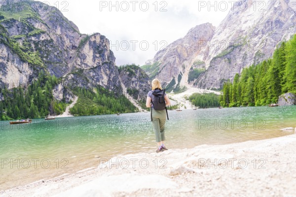 A woman enjoys the view from a lake shore of the majestic mountains all around, Pragser Wildsee, South Tyrol, Dolomites, Italy