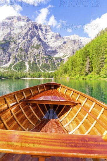 An empty wooden boat on a clear mountain lake with a view of steep rocks and wooded hills, Pragser Wildsee, South Tyrol, Dolomites, Italy