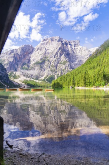 Clear lake with mountain reflection and boats, surrounded by dense forest, Pragser Wildsee, South Tyrol, Dolomites, Italy
