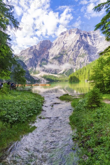 A clear mountain lake surrounded by impressive mountains and dense forest under a partly cloudy sky, Pragser Wildsee, South Tyrol, Dolomites, Italy