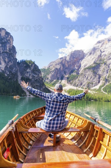 Man spreads his arms with joy on a boat on a mountain lake, Pragser Wildsee, South Tyrol, Dolomites, Italy