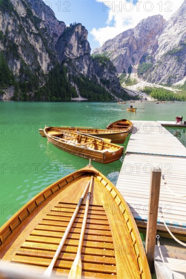 Several wooden boats are moored to a jetty on a calm, emerald-green mountain lake, Lake Braies, South Tyrol, Dolomites, Italy