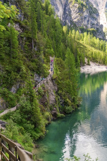 A narrow path winds along a steep slope with a view of an emerald green lake, Pragser Wildsee, South Tyrol, Dolomites, Italy