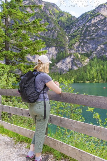 Person looking from a wooden fence at a mountain lake, surrounded by nature, Lake Braies, South Tyrol, Dolomites, Italy
