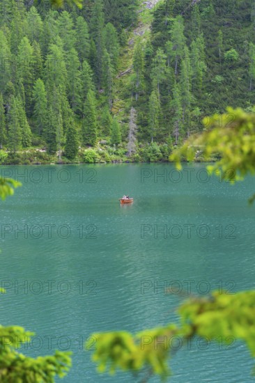 A small red boat on a turquoise-blue lake, surrounded by dense forest, Pragser Wildsee, South Tyrol, Dolomites, Italy