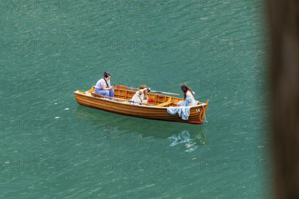 Three people in a wooden boat, floating relaxed on the water, in peaceful surroundings, Lake Braies, South Tyrol, Dolomites, Italy