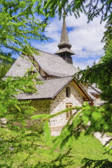 An idyllically situated church with a pointed tower, surrounded by dense vegetation, Lake Braies, South Tyrol, Dolomites, Italy