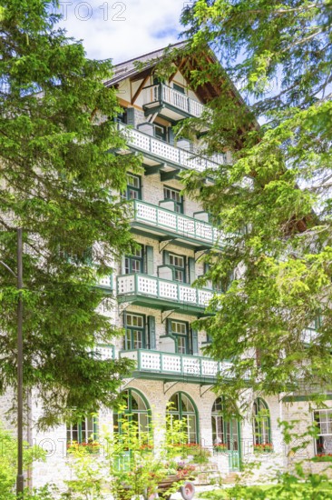 A white hotel building with balconies surrounded by green trees, Lake Braies, South Tyrol, Dolomites, Italy
