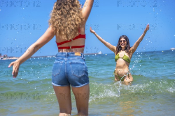 Two cheerful young women enjoying their summer vacation, splashing water in the crystal clear sea