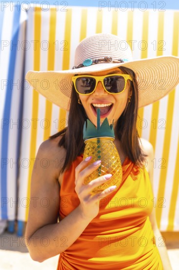 Young woman wearing sunglasses and a straw hat enjoying a refreshing pineapple juice at the beach