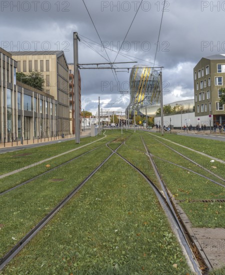 Grass-covered tram tracks crossing in bordeaux city center, with the cité du vin museum in the background, showcasing urban development and sustainable transportation