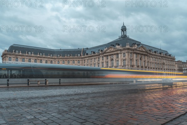 Long exposure photo of a tram passing by the stock exchange palace of bordeaux, france, in a cloudy evening