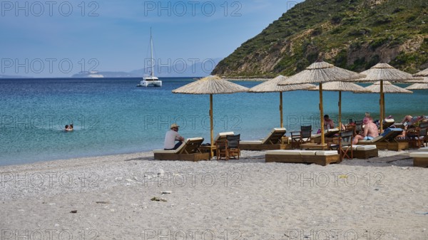 Kamari beach, Relaxed beach with sun loungers and parasols, Sailboat on the horizon in clear blue water, Kefalos, Kos, Dodecanese, Greek Islands, Greece