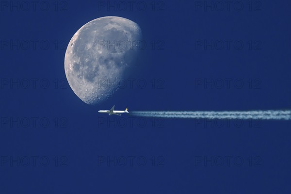 Aeroplane with contrails in front of a waning moon in the early morning sky, Bavaria, Germany