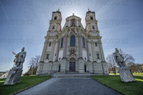 East tower of the baroque basilica backlit, in front the two church patrons, St Alexander on the left and St Theodore on the right, Ottobeuren Monastery, Ottobeuren, Unterallgäu, Bavaria, Germany