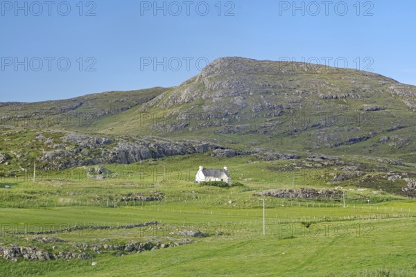 Small house in a green valley surrounded by mountains under clear skies, Isle of Barra, Hebrides, Scotland, United Kingdom