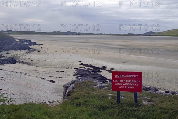 Empty beach with a warning sign in the foreground, surrounded by dunes and a wide sky, airport, runway, tides, Isle of Barra, Hebrides, Scotland, United Kingdom