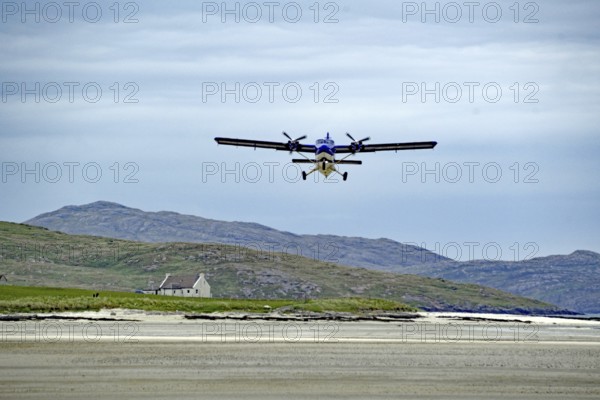 Low flying aeroplane over a runway in mountain landscape with cloudy sky, Isle of Barra, Hebrides, Scotland, Great Britain