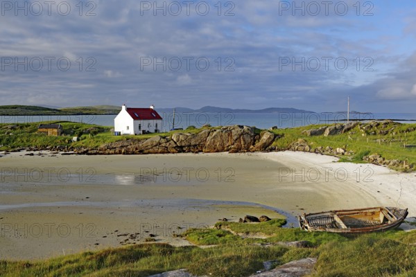 Boat wreck on a sandy beach with a white house and rocks in the background, Isle of Barra, Hebrides, Scotland, United Kingdom