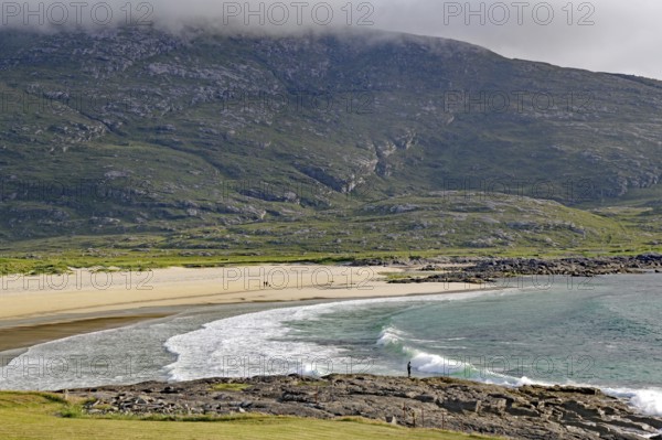 Expansive coastline with beach and waves against a mountain backdrop under a cloudy sky, Castlebay, Isle of Barra, Hebrides, Scotland, United Kingdom