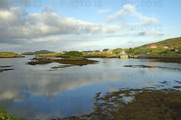 Calm lake in idyllic surroundings with clouds and houses in the background, evening mood, Isle of Barra, Hebrides, Scotland, Great Britain