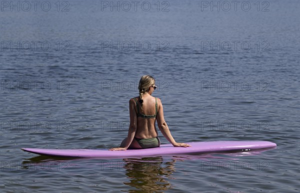 Woman, blonde, in bikini, sitting on board, surfboard, surfboard, purple, back, from behind, relaxed, bathing lake, lake, Schwaltenweiher near Seeg, Ostallgäu, Allgäu, Swabia, Bavaria, Germany