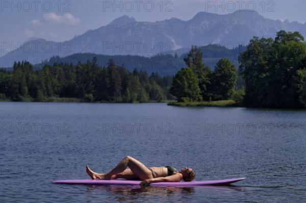 Woman, blonde, in bikini, lying on board, surfboard, surfboard, purple, relaxed, bathing lake, lake, Schwaltenweiher near Seeg, Allgäu Alps, East Allgäu, Allgäu, Swabia, Bavaria, Germany