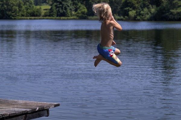 Boy, 6 years, blond, jumping from wooden footbridge, footbridge into the water, bathing lake, lake, Schwaltenweiher near Seeg, Ostallgäu, Allgäu, Swabia, Bavaria, Germany