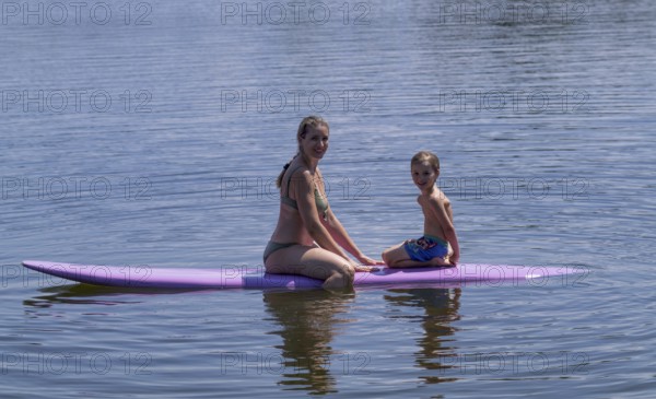 Mother, woman, blonde, in bikini and son, boy, 6 years, sitting on board, surfboard, surfboard, violet, back, from behind, relaxed, bathing lake, lake, Schwaltenweiher near Seeg, Ostallgäu, Allgäu, Swabia, Bavaria, Germany