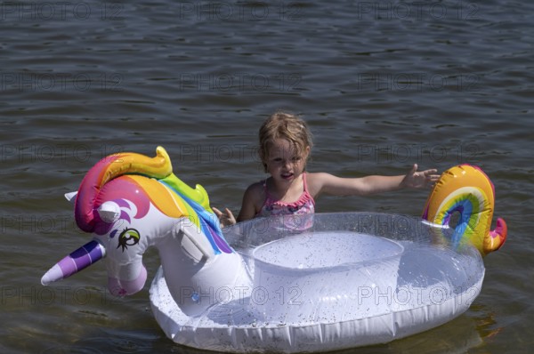 Girl, 3 years, blonde, playing with unicorn, swimming ring, inflatable, in the water, bathing lake, lake, Schwaltenweiher near Seeg, Ostallgäu, Allgäu, Swabia, Bavaria, Germany