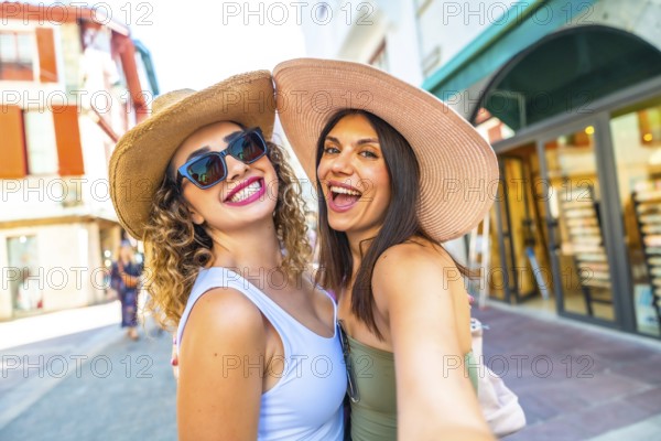Two happy female tourists with straw hats and sunglasses taking a selfie while enjoying their vacation