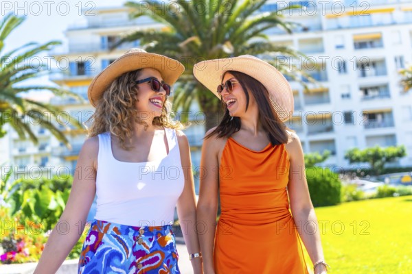 Two female tourists wearing sunglasses and sun hats walk and talk together while enjoying their vacation