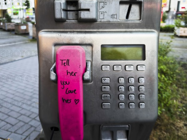 Telephone receiver of a Telekom payphone with the inscription Tell her you love her in Wuppertal, Germany
