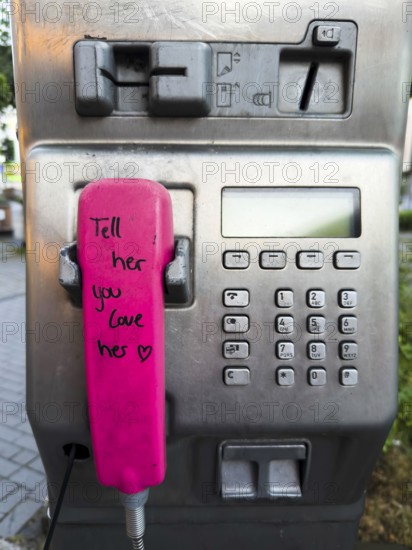 Telephone receiver of a Telekom payphone with the inscription Tell her you love her in Wuppertal, Germany