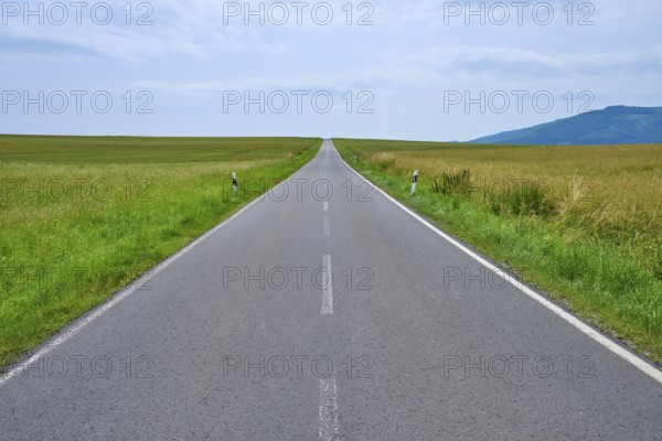 A straight country road leads through wide fields to distant hills under a cloudy sky, Orferode, town of Bad Sooden-Allendorf, Werra-Meißner-Kreis, Hesse, Germany
