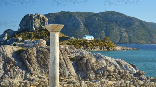 Ancient column and stones in front of island with chapel, blue sky in the background, Agios Stefanos Beach, Agios Stefanos Basilica, Chapel Agios Nikolaos, Kastri Island, Kos, Dodecanese, Greek Islands, Greece