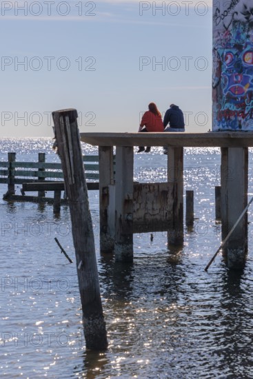 Man and woman sitting on a concrete platform at the base of the graffiti, covered Broadwater Beach Marina Light in Biloxi, MS
