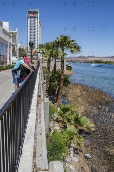 Couple looking at cell phone on sidewalk overlooking jet ski activity on the Colorado River in Laughlin, Nevada