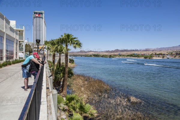 Couple looking at cell phone on sidewalk overlooking jet ski activity on the Colorado River in Laughlin, Nevada