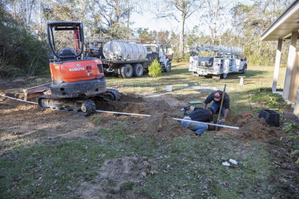Workers installing pipe connecting new water well to house plumbing in rural area of Gulfport, Mississippi, USA
