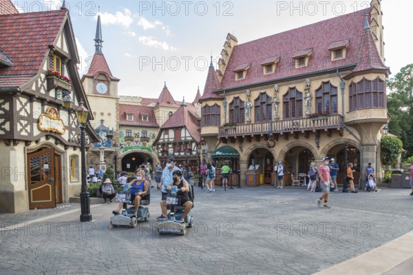 Masked park guests walking and riding scooters through the Germany pavilion of Epcot at Walt Disney World in Orlando, Florida