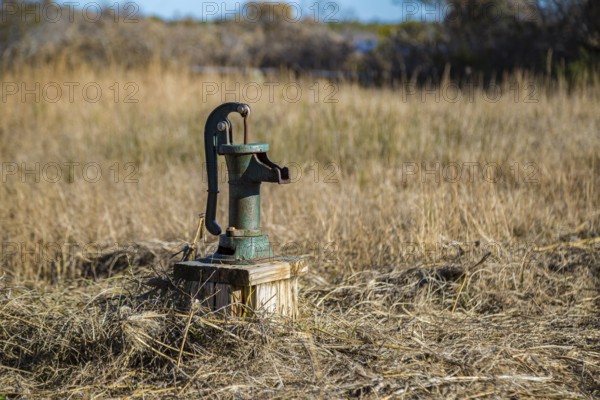 Old fashioned manual hand pump on water well in grassy field