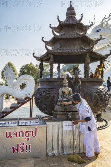 Worker cleaning Buddhist statue in fron of the Guan Yin (Goddess of Mercy) statue at Wat Huay Pla Kang Temple in Chiang Rai province of Northern Thailand