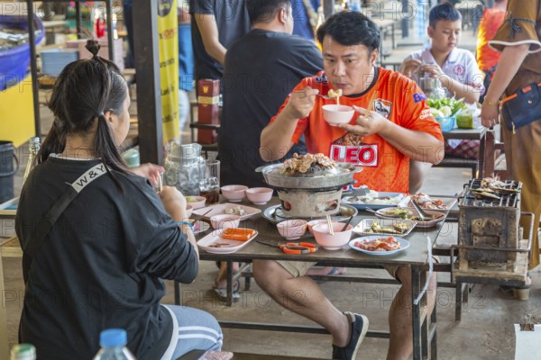 Thai couple cooking on a hot pot and eating at a buffet style outdoor restaurant in Chiang Rai province of Northern Thailand