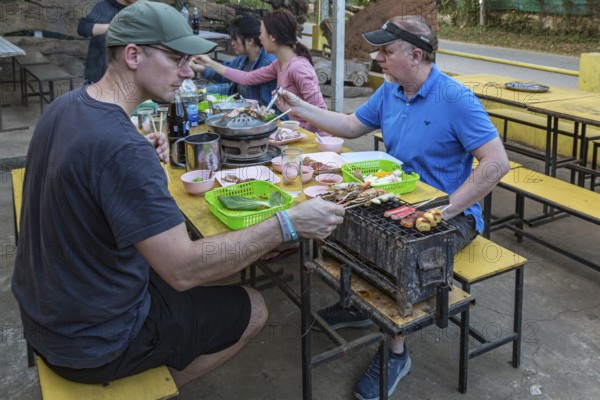 Male American missionaries cooking their food on a charcoal grill and hot pot at a buffet style outdoor restaurant in Chiang Rai province of Northern Thailand