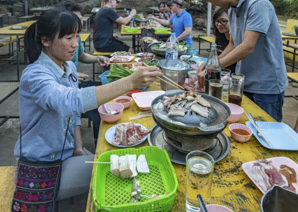 Thai woman cooking fish on a charcoal hot pot at a buffet style outdoor restaurant in Chiang Rai province of Northern Thailand