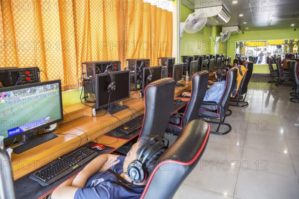 Thai men and boys watching online sports and playing video games online at an Internet gaming business in Chiang Rai, Thailand